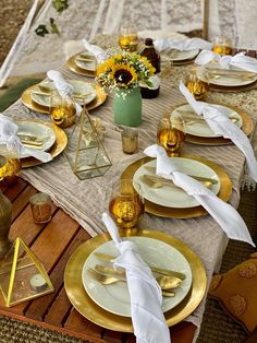 the table is set with gold and white plates, napkins, and vases