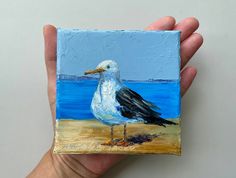 a painting of a seagull is being held by a person's hand