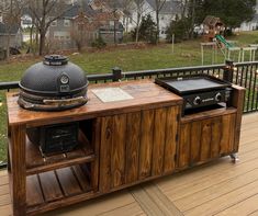 an outdoor bbq grill on a deck next to a wooden table with two drawers