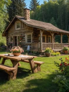 a wooden picnic table sitting in front of a log cabin with flowers on the lawn