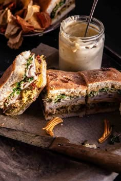 a sandwich cut in half sitting on top of a cutting board next to a jar of dressing