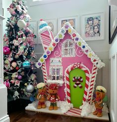 a pink gingerbread house decorated with candy canes and christmas decorations next to a tree