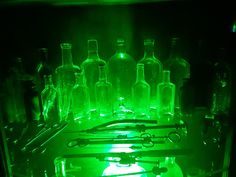 several bottles are lit up in the dark with green light shining on them, and there is an assortment of utensils