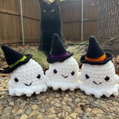 three crocheted marshmallows with witches hats on them sitting in front of a black cat