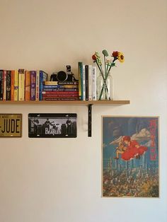 some books are sitting on a shelf next to pictures and vases with flowers in them