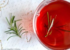 a cup filled with red liquid next to a sprig of rosemary