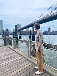 a man standing on a pier next to the water and a bridge in the background