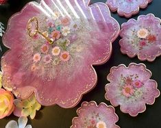 pink and white flowers are sitting on a table next to some glass plates with gold handles