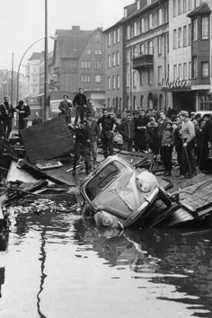 an old photo of people standing around a car that has been partially submerged in water