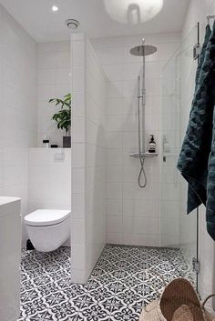 a white bathroom with black and white tile flooring, a toilet and shower head mounted to the wall