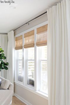 a living room with white curtains and a couch in front of the window that is closed