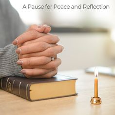 a woman holding her hands on top of a book next to a candle and cell phone