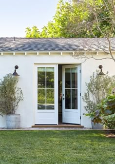 a white house with an open front door and two potted plants on the lawn