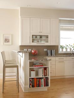 a kitchen with white cupboards and an island in the middle is filled with books