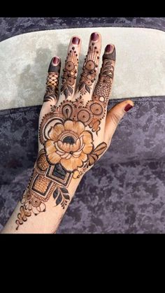 a woman's hand with henna tattoos on it and an orange flower in the middle