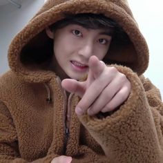 a young man in a brown teddy bear jacket pointing at the camera with his finger