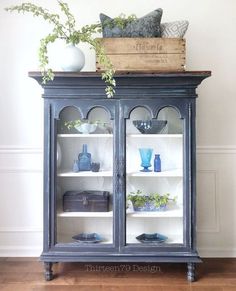 a blue china cabinet with glass doors and shelves filled with vases, plants and other decorative items