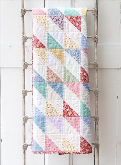 a multicolored quilt hanging on the side of a white wooden wall next to a ladder