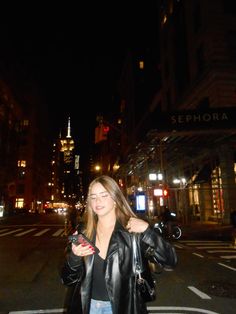 a woman standing in the middle of a street at night with her hand on her hip