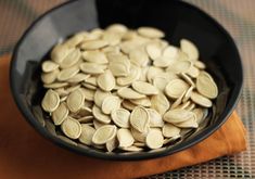 a black bowl filled with pumpkin seeds on top of a wooden table next to an orange napkin