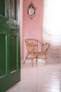 a wicker chair sitting in front of a pink wall with a mirror above it