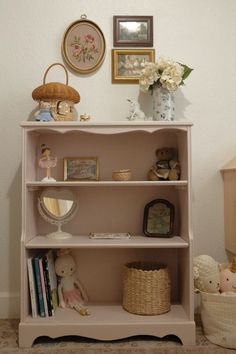 a pink book shelf with pictures and stuffed animals on it's shelves next to a basket