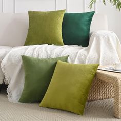 four green and white pillows sitting on top of a couch next to a wicker table