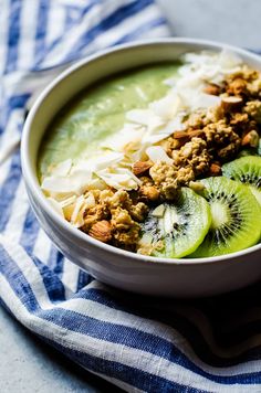 a bowl filled with green smoothie and topped with kiwis, nuts and coconut