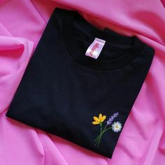 a black t - shirt with yellow and white flowers on it sitting on pink fabric