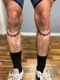 a man with tattoos on his legs standing on a wooden floor