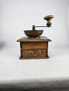 an old fashioned grinder sitting on top of a wooden box next to a white wall