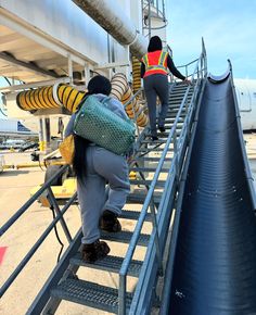 three people are climbing up the stairs to an air port jetway that is being loaded with supplies