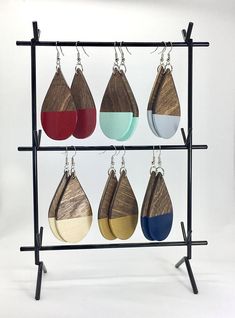 six pairs of wooden tear earrings hanging on a black metal rack with four different colors