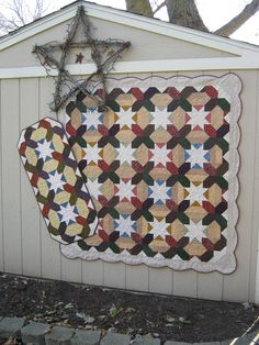 two quilts hanging on the side of a white building next to a star decoration