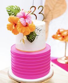 a white and pink cake with flowers on top sitting on a table next to other desserts