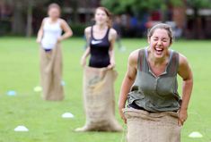 three women are laughing in the grass with bags on their heads and one woman is wearing a black tank top