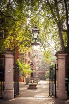 an iron gate with a lamp post and bench in front of it on a sunny day