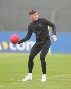 a man holding a red soccer ball on top of a grass covered field in the rain