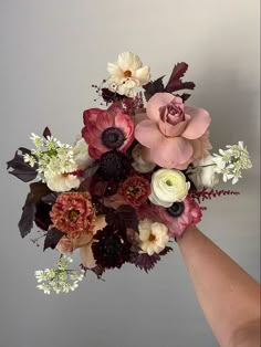 a hand holding a bouquet of flowers on top of a white wall with grey walls behind it