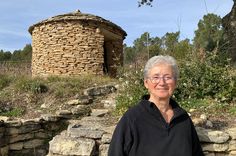 an older woman standing in front of a stone structure