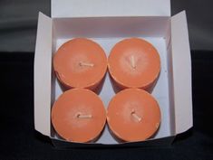 four orange candles sitting in a white box