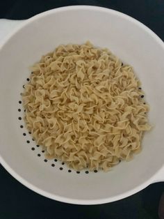 a white bowl filled with noodles on top of a black countertop next to a wooden spoon