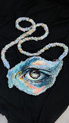 a black shirt with an eye on the front and beaded necklace hanging from it