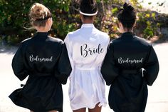 three bridesmaids in black and white robes walk down the street together with their backs to each other