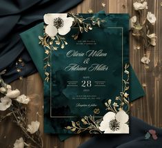 an elegant wedding card with white flowers and gold foil on green paper, surrounded by black satin