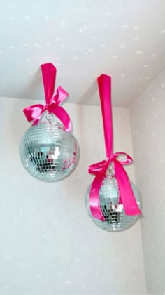 two disco ball ornaments with pink ribbons hanging from the ceiling