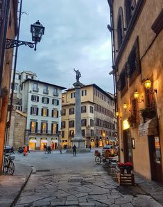 people are walking around in an old european city at night time, with tall buildings and cobblestone streets