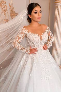 a woman wearing a wedding dress with long sleeves and a veil on her head is posing for the camera