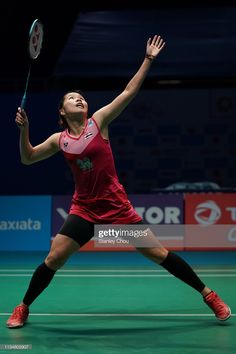 a woman in red shirt and black shorts playing tennis on green court with dark background