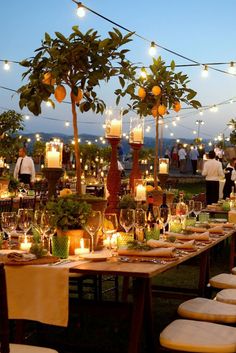 an outdoor dinner setup with candles and fruit trees